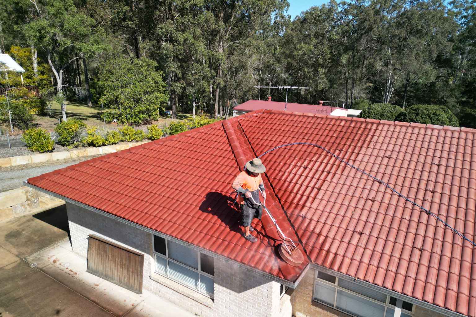 Roofing professional cleaning a red tiled roof in North Brisbane